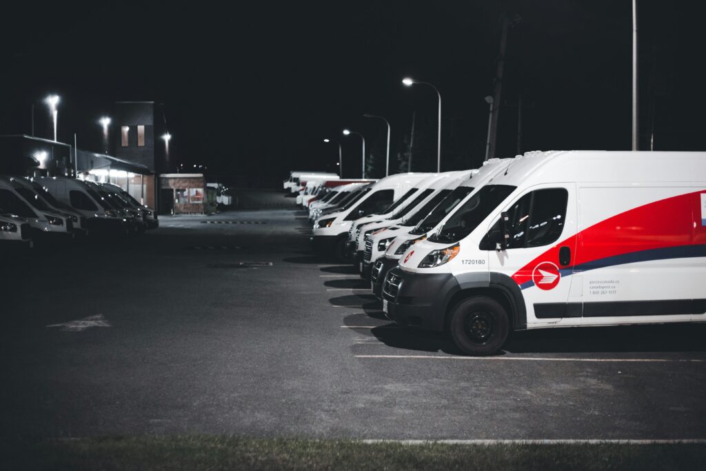 A lineup of white and red delivery vans parked in a lot under streetlights at night.