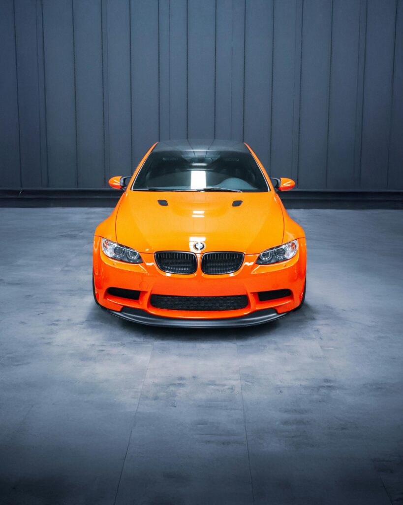 Front view of an orange sports car in a modern indoor setting, showcasing sleek design.